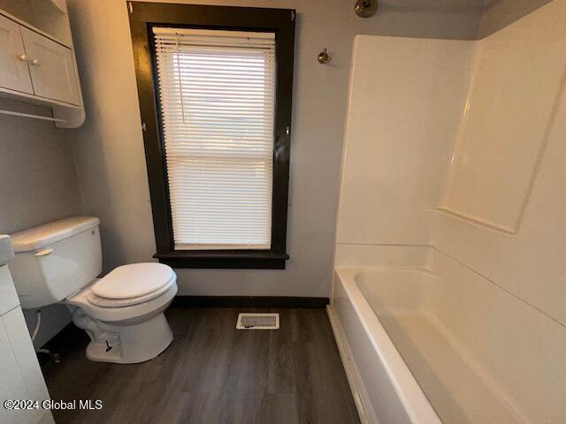 bathroom with hardwood / wood-style floors, toilet, and washtub / shower combination