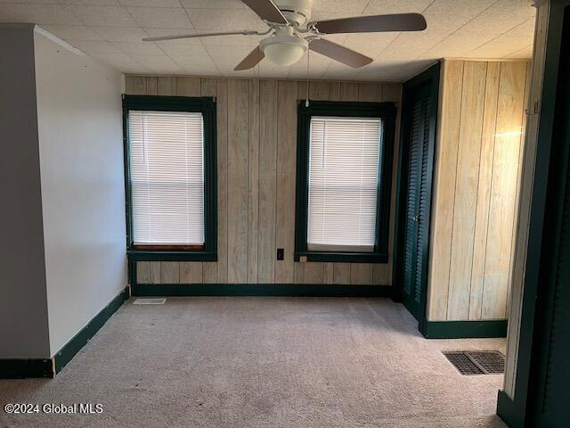 carpeted spare room with ceiling fan and wood walls