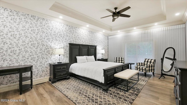 bedroom featuring light hardwood / wood-style floors, ornamental molding, a tray ceiling, and ceiling fan