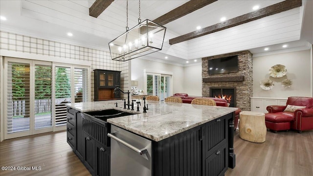 kitchen featuring a center island with sink, dishwasher, dark hardwood / wood-style floors, pendant lighting, and a stone fireplace