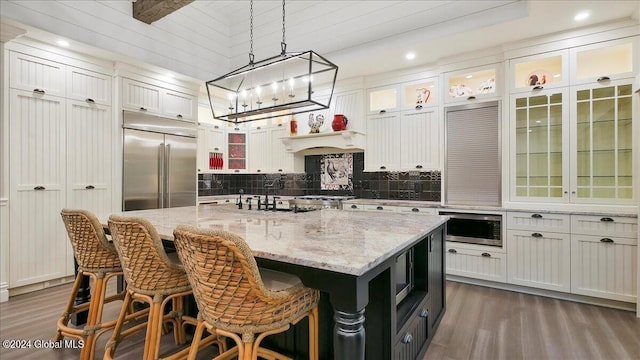 kitchen with a kitchen island, white cabinetry, wood-type flooring, built in appliances, and pendant lighting