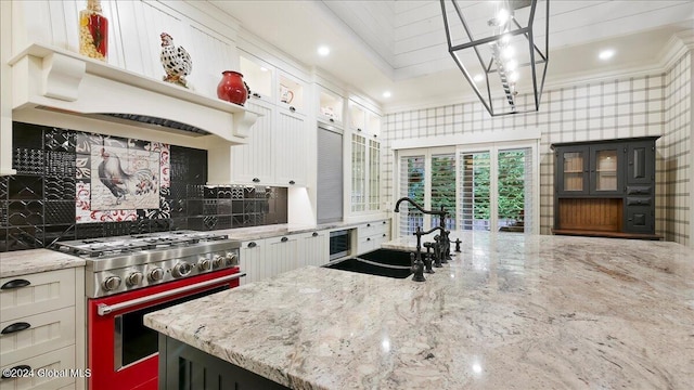 kitchen with hanging light fixtures, light stone counters, white cabinetry, stainless steel stove, and sink