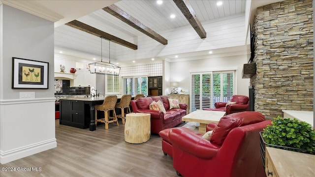 living room featuring beam ceiling, a stone fireplace, crown molding, light hardwood / wood-style floors, and a notable chandelier