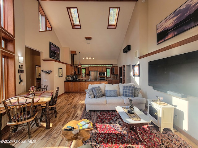 living room with a skylight, light wood-type flooring, and high vaulted ceiling