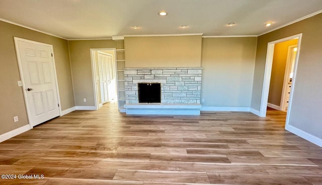 unfurnished living room featuring a stone fireplace, ornamental molding, and light hardwood / wood-style floors