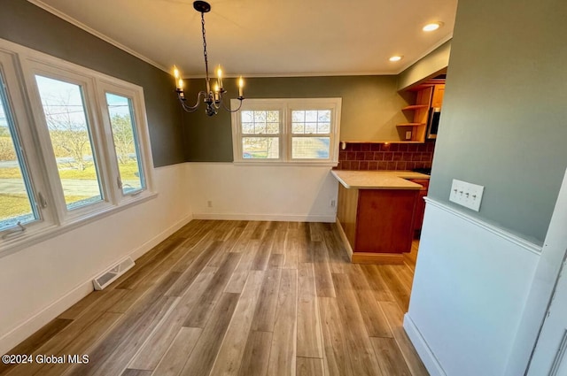 unfurnished dining area with ornamental molding, a healthy amount of sunlight, an inviting chandelier, and light wood-type flooring