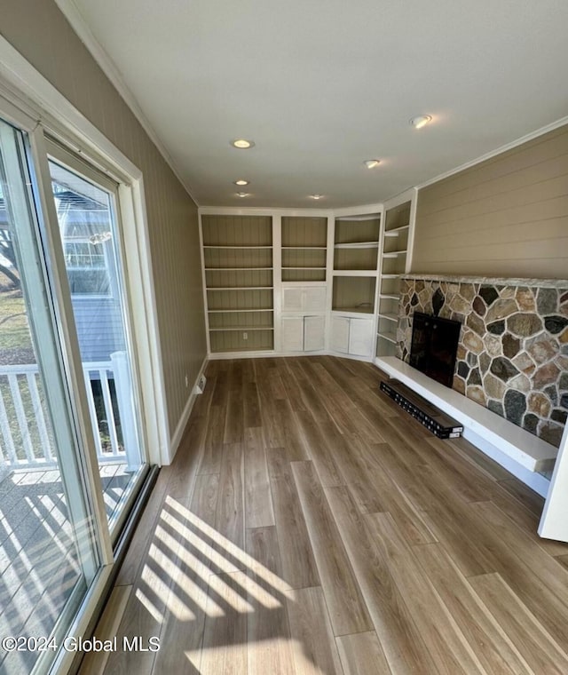 unfurnished living room featuring crown molding, a stone fireplace, wood-type flooring, and a healthy amount of sunlight