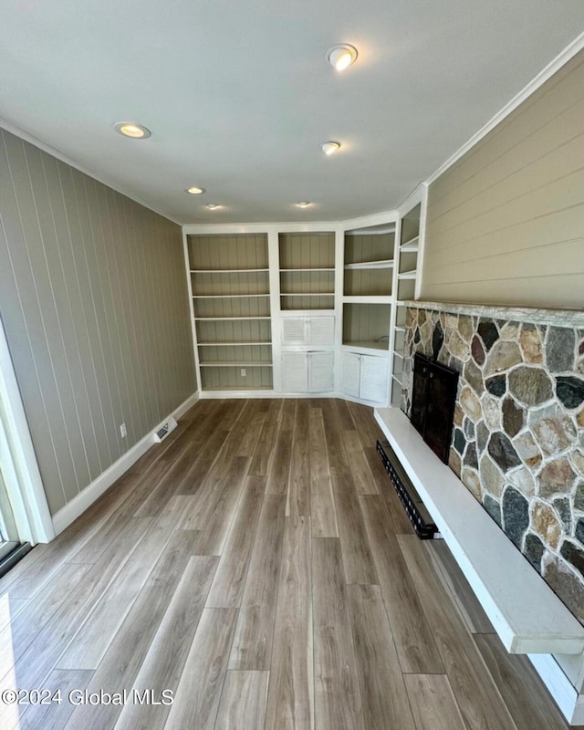 unfurnished living room with a fireplace, wooden walls, wood-type flooring, ornamental molding, and built in shelves