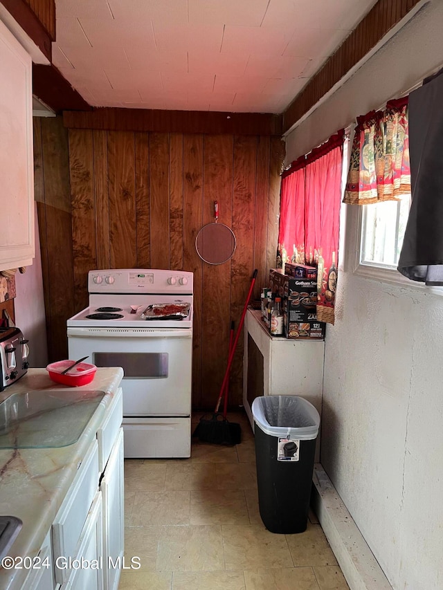 kitchen with electric range, white cabinets, and wooden walls