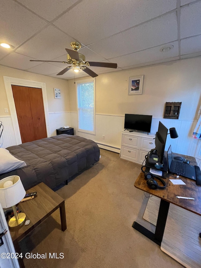 carpeted bedroom with a drop ceiling, a baseboard radiator, and ceiling fan