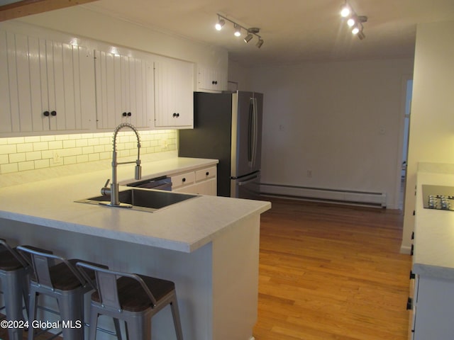 kitchen with white cabinets, a sink, decorative backsplash, a peninsula, and baseboard heating