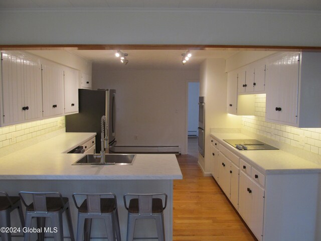 kitchen with tasteful backsplash, a breakfast bar, kitchen peninsula, white cabinetry, and light hardwood / wood-style flooring