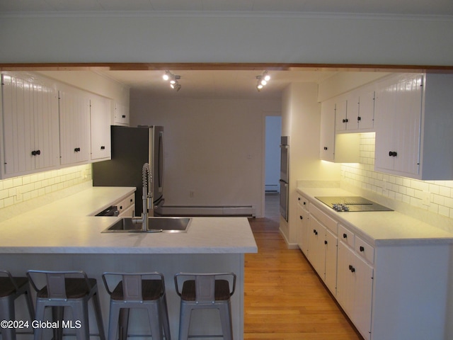 kitchen featuring baseboard heating, a sink, decorative backsplash, a peninsula, and freestanding refrigerator