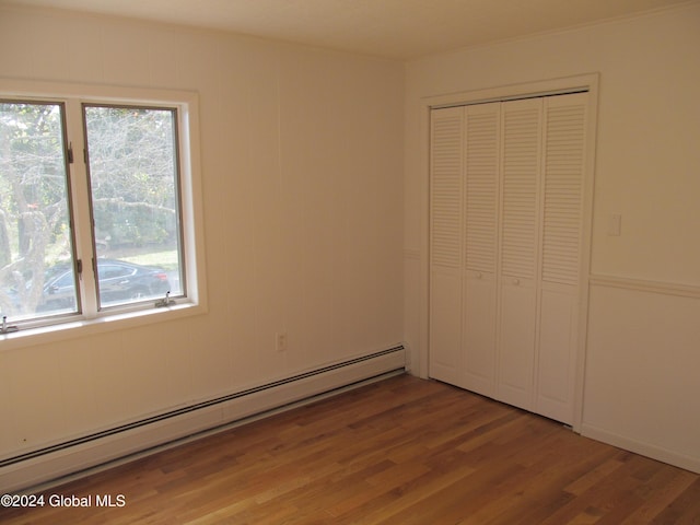 unfurnished bedroom featuring a baseboard radiator, light wood-style flooring, a closet, and multiple windows