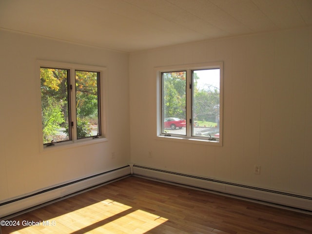 unfurnished room featuring baseboard heating, a wealth of natural light, and wood finished floors