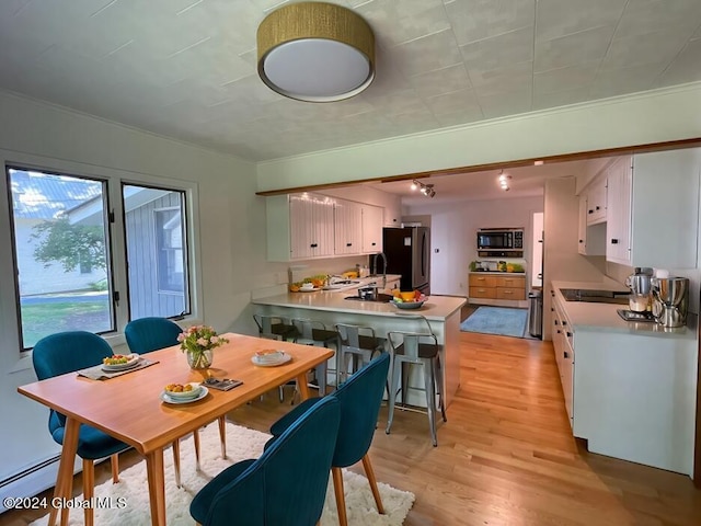 dining area with a baseboard radiator, light wood-style floors, and ornamental molding