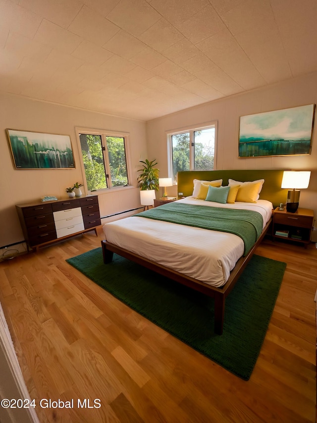 bedroom with a baseboard heating unit and wood finished floors