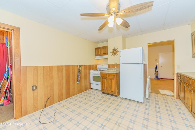 kitchen featuring white appliances, ceiling fan, and wood walls