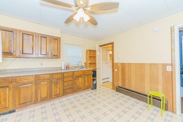 kitchen with a baseboard heating unit, wooden walls, sink, and ceiling fan