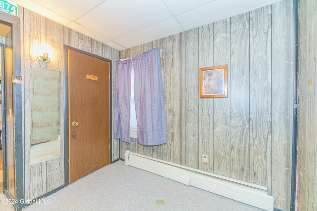 interior space featuring baseboard heating, wooden walls, a drop ceiling, and carpet