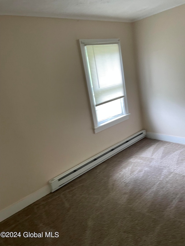 empty room with a baseboard heating unit and dark colored carpet