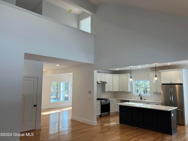 kitchen featuring a kitchen island, a wealth of natural light, stainless steel appliances, a high ceiling, and decorative light fixtures