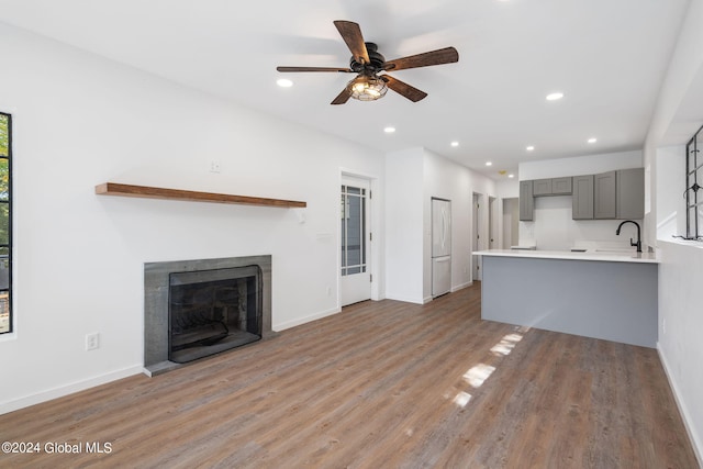 unfurnished living room with light wood-type flooring, ceiling fan, and sink