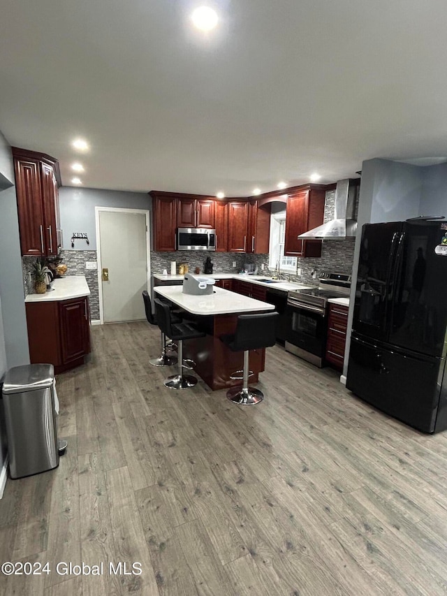 kitchen featuring tasteful backsplash, range, black fridge, light hardwood / wood-style floors, and wall chimney exhaust hood