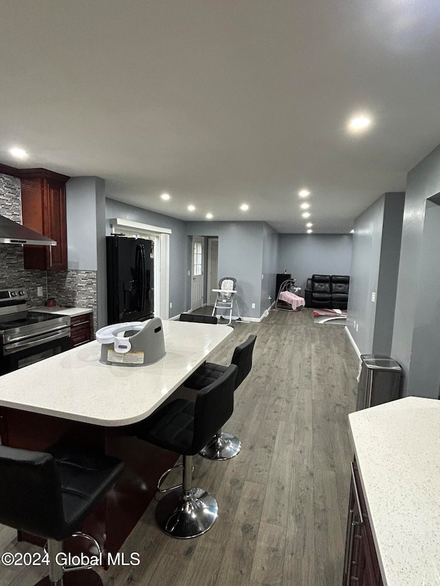 kitchen with wood-type flooring, electric stove, backsplash, a breakfast bar area, and black refrigerator