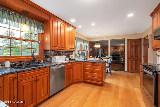 kitchen featuring stainless steel appliances, sink, decorative light fixtures, light wood-type flooring, and tasteful backsplash