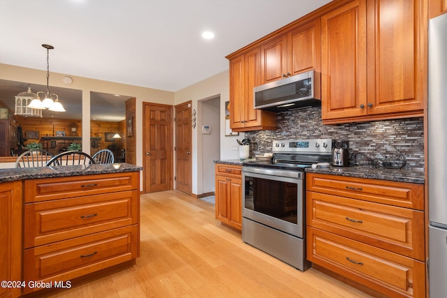 kitchen with tasteful backsplash, light hardwood / wood-style floors, stainless steel appliances, dark stone counters, and a notable chandelier