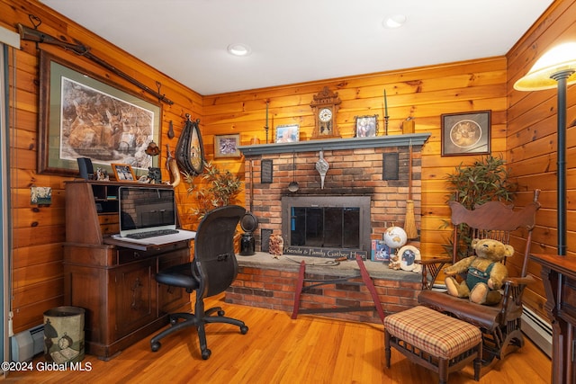 office with light hardwood / wood-style flooring, wooden walls, and a brick fireplace