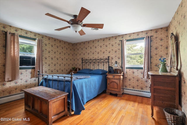 bedroom featuring light hardwood / wood-style floors, multiple windows, baseboard heating, and ceiling fan