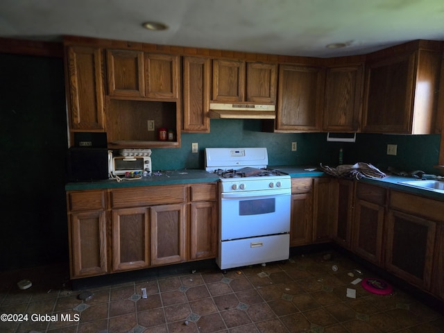 kitchen with dark tile patterned floors, sink, and white gas range