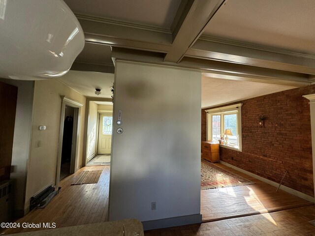 corridor with brick wall, ornamental molding, beamed ceiling, and wood-type flooring