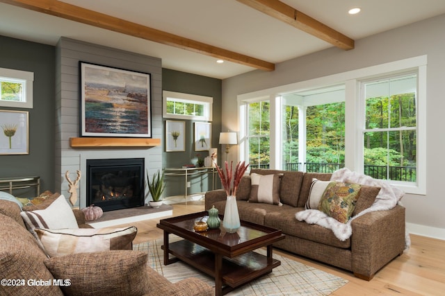 living room featuring a large fireplace, beamed ceiling, a healthy amount of sunlight, and light hardwood / wood-style floors