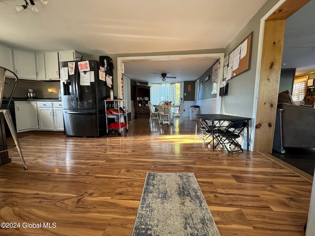 interior space with white cabinetry, ceiling fan, black fridge, and hardwood / wood-style floors