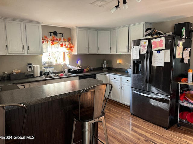 kitchen with sink, light hardwood / wood-style floors, fridge with ice dispenser, white cabinets, and a breakfast bar