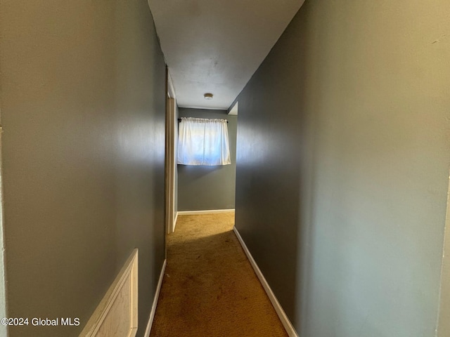 hall with visible vents, dark carpet, and baseboards