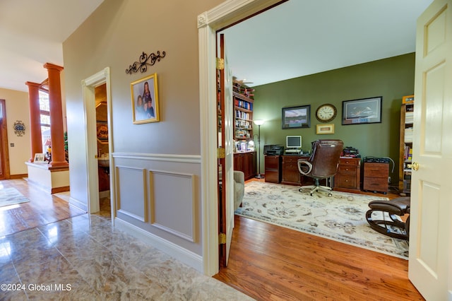 corridor with light wood-type flooring and decorative columns