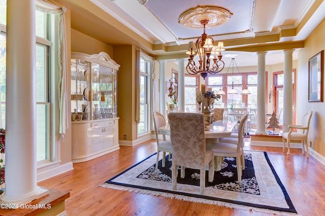 dining room featuring ornate columns, ornamental molding, an inviting chandelier, a raised ceiling, and light hardwood / wood-style floors