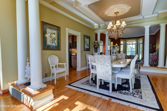 dining space featuring a chandelier, a tray ceiling, decorative columns, ornamental molding, and light hardwood / wood-style floors