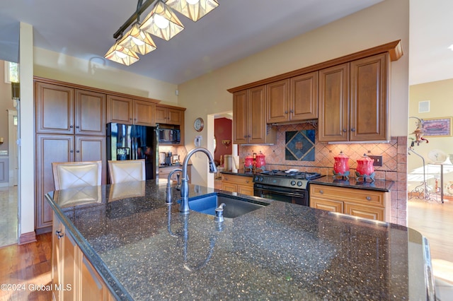 kitchen with hanging light fixtures, light wood-type flooring, dark stone countertops, black appliances, and sink