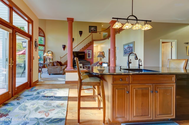 kitchen with black dishwasher, sink, a breakfast bar area, hanging light fixtures, and light hardwood / wood-style flooring