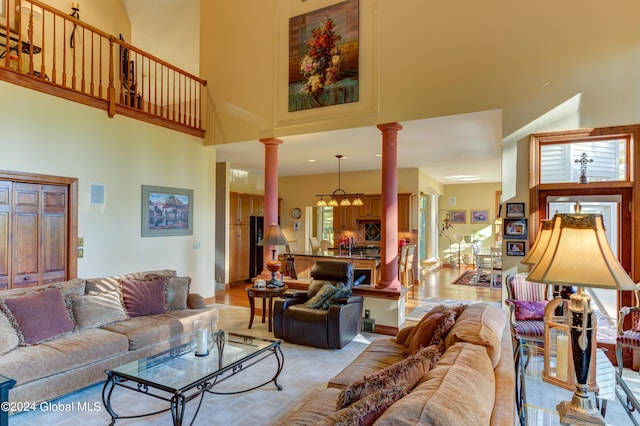 living room featuring ornate columns, a towering ceiling, an inviting chandelier, and light wood-type flooring