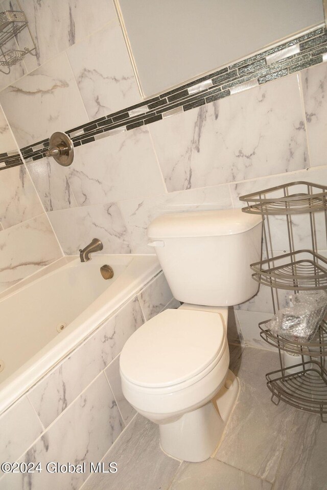 full bath featuring toilet, marble look tile flooring, and tile walls