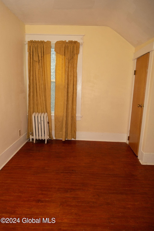 spare room featuring lofted ceiling, dark wood-type flooring, and radiator heating unit