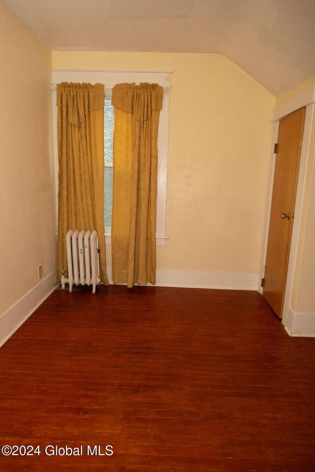 additional living space featuring radiator, dark wood-style floors, baseboards, and vaulted ceiling