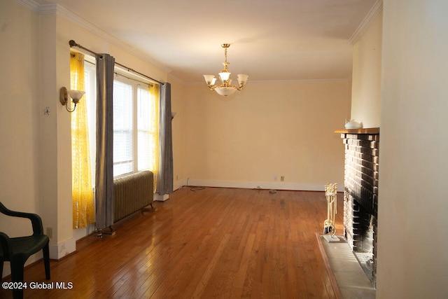 unfurnished dining area featuring wood-type flooring, a fireplace, radiator, crown molding, and a notable chandelier