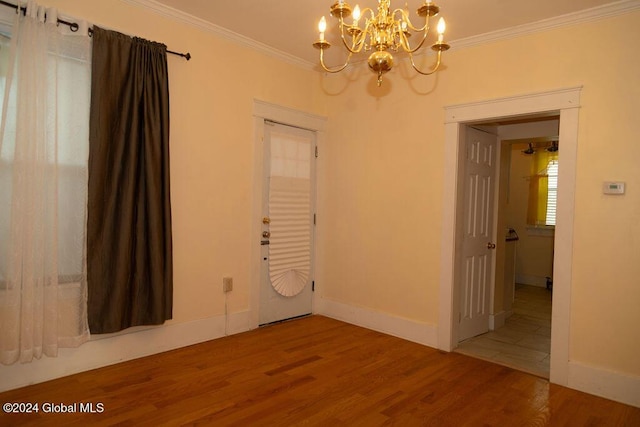 spare room with a chandelier, wood finished floors, ornamental molding, and baseboards